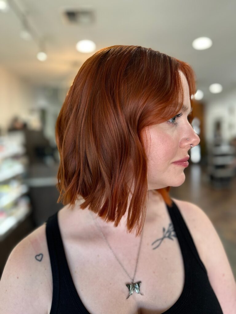 A woman showcases a textured copper red long bob hairstyle with subtle layers and a soft curtain fringe.
