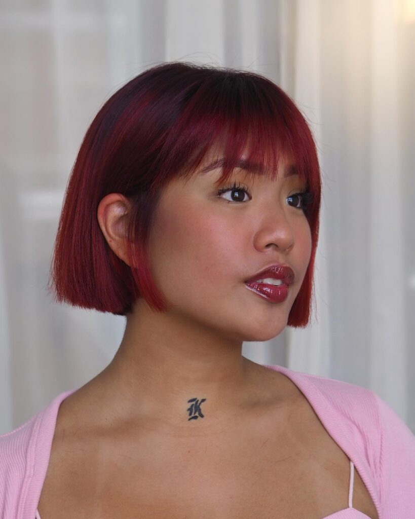 A woman showcases a straight, chin-length bright tangerine red asymmetrical bob hairstyle with neon orange highlights.