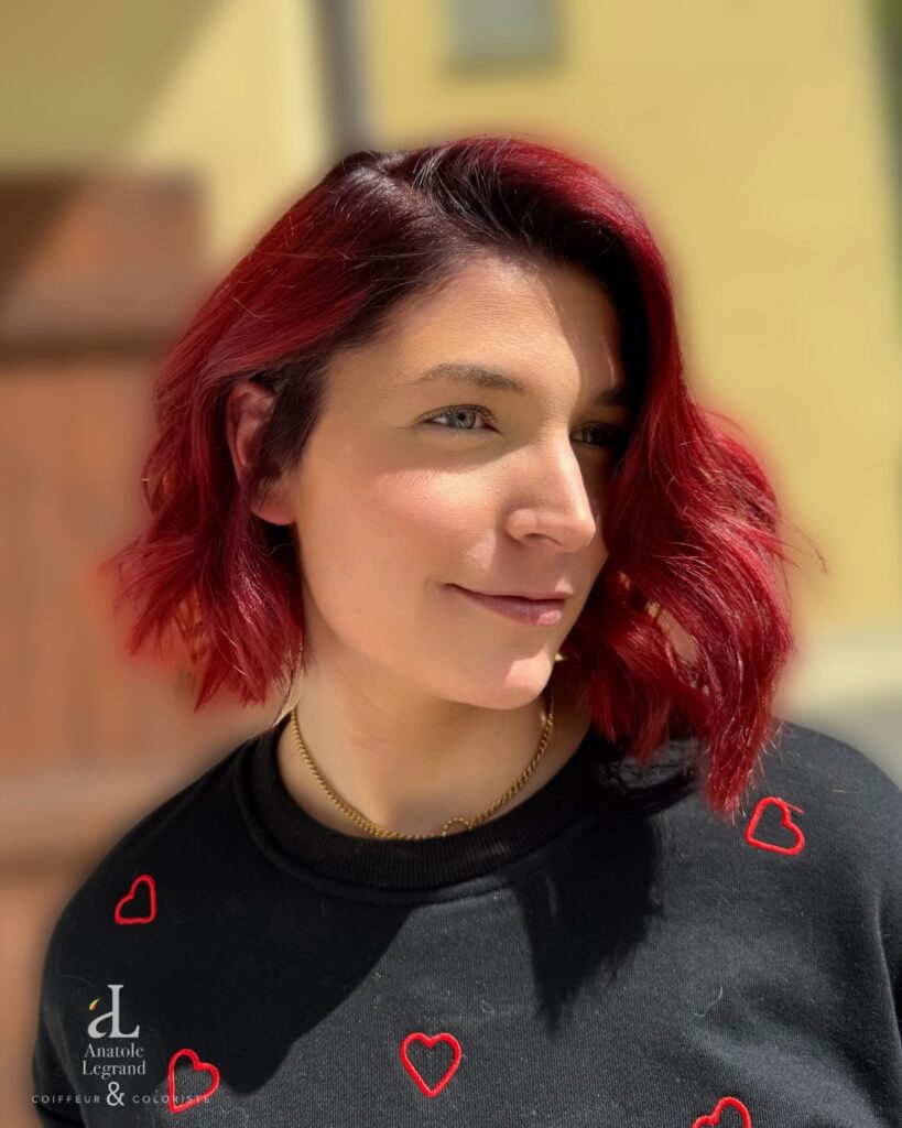 A side profile view of a woman showcasing a bright ginger red pixie bob hairstyle with short choppy layers and a wispy fringe.