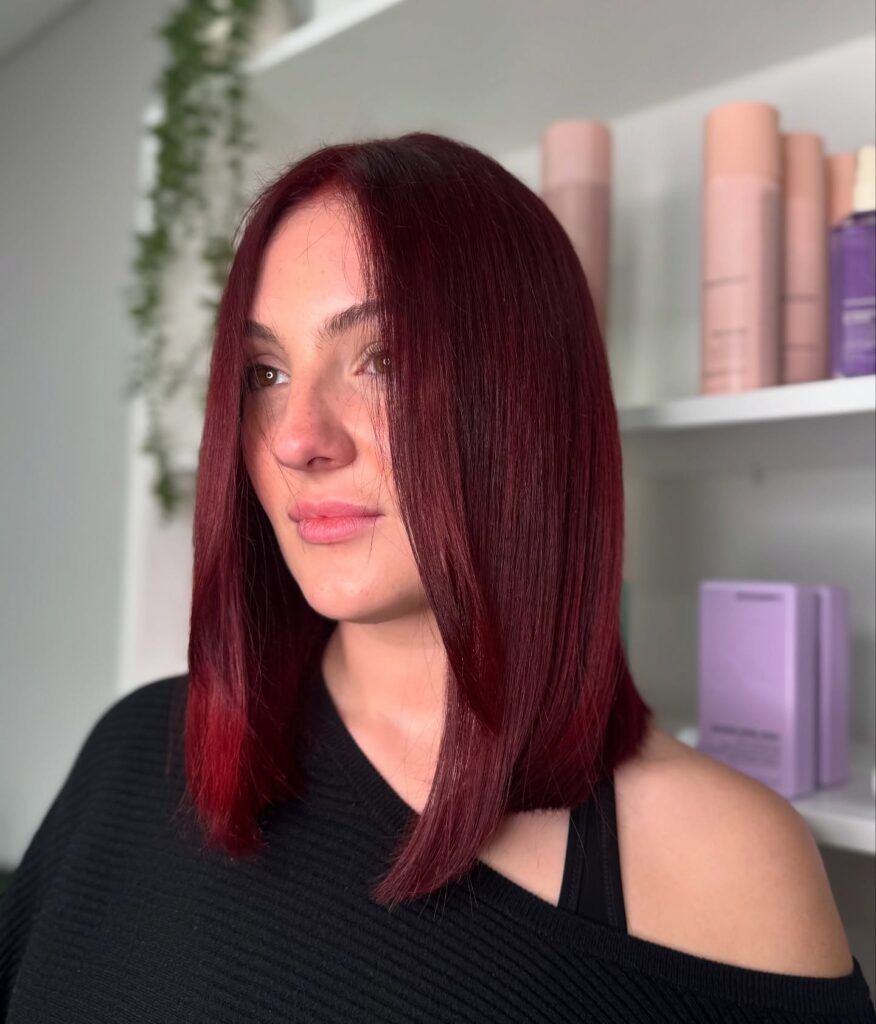 A woman features a sleek, straight maroon red long bob hairstyle cut to the collarbone with a middle part.