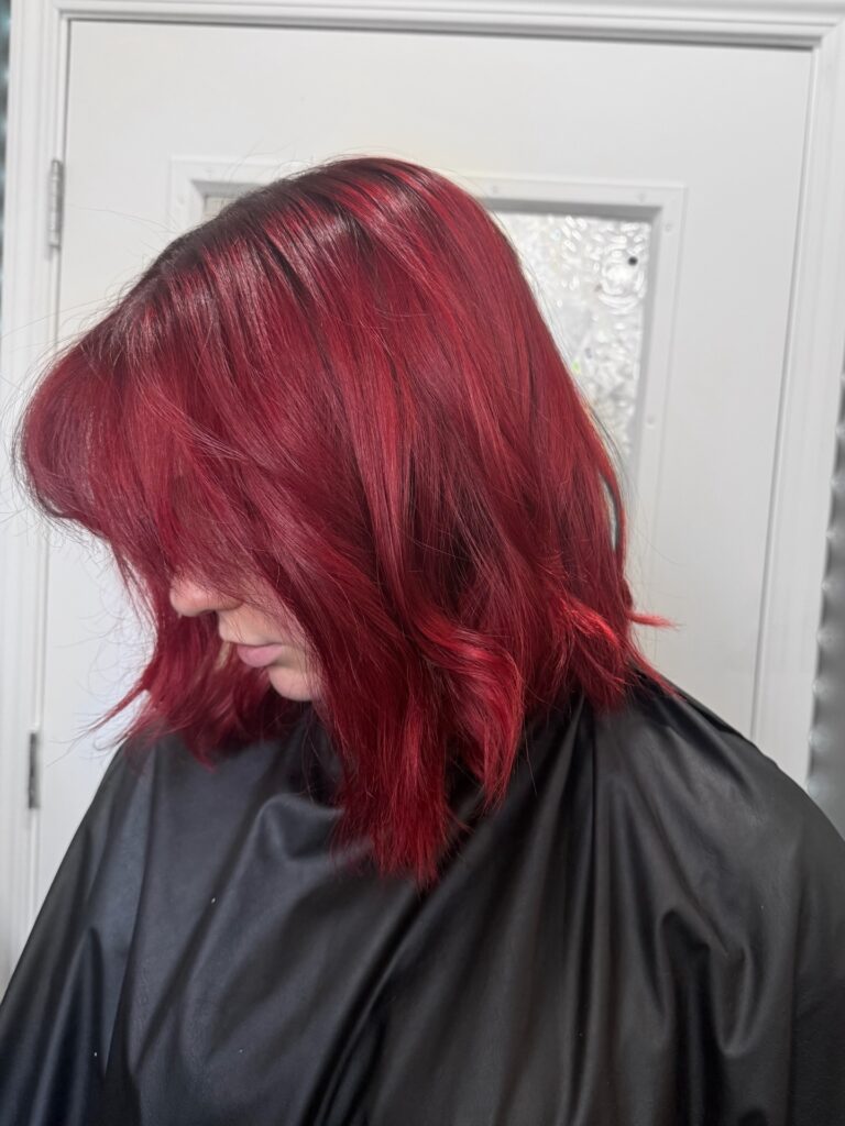 A woman showcases a heavily texturized, shoulder-length cherry red long bob hairstyle with a full side fringe and messy waves.