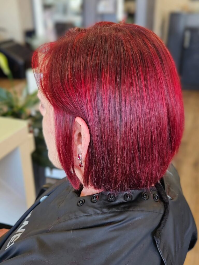A side and back view of a woman featuring a straight, chin-length ruby red choppy bob hairstyle with texturized ends.