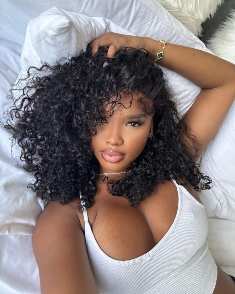 Voluminous curly long bob with tight curls and a deep side part.