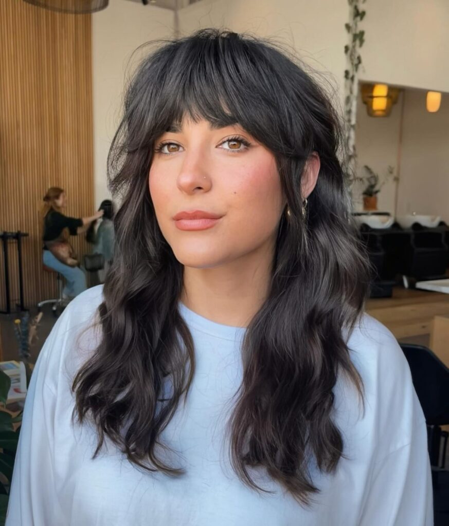 A woman with a shoulder-length shaggy dark brown bob with heavy wavy texture and thick curtain bangs.
