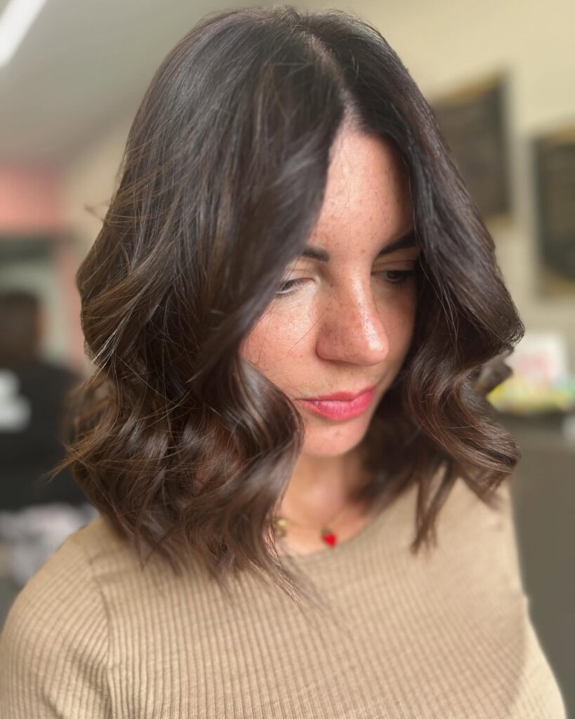 Shoulder length brunette lob with soft glossy waves and subtle layers.