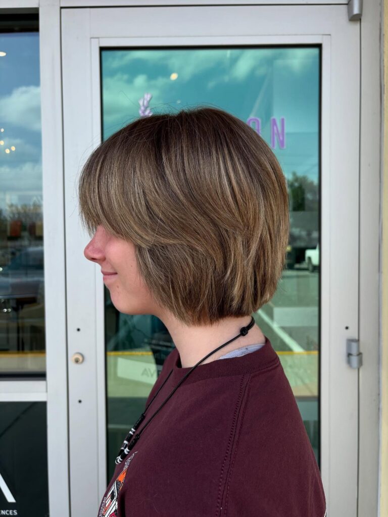 A woman viewed in side profile wearing a light ash brown choppy bob with face-framing blonde highlights.