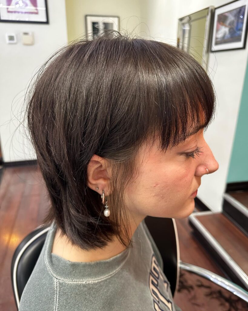 A woman shown in side profile sporting a dark brunette shaggy bob with choppy layers and light wispy bangs.