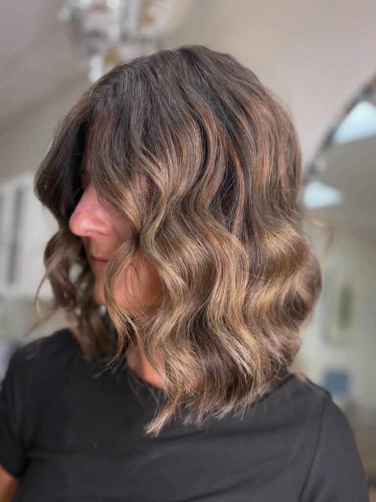 A woman viewed from the side profile showing off a dark brunette wavy long bob with subtle caramel highlights.