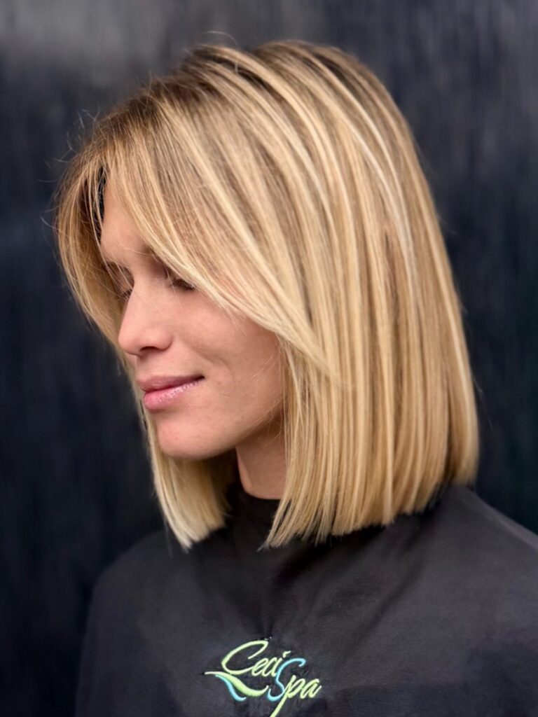 A woman looking forward with a middle parted caramel blonde chin length bob featuring soft choppy layers and a texturized finish.
