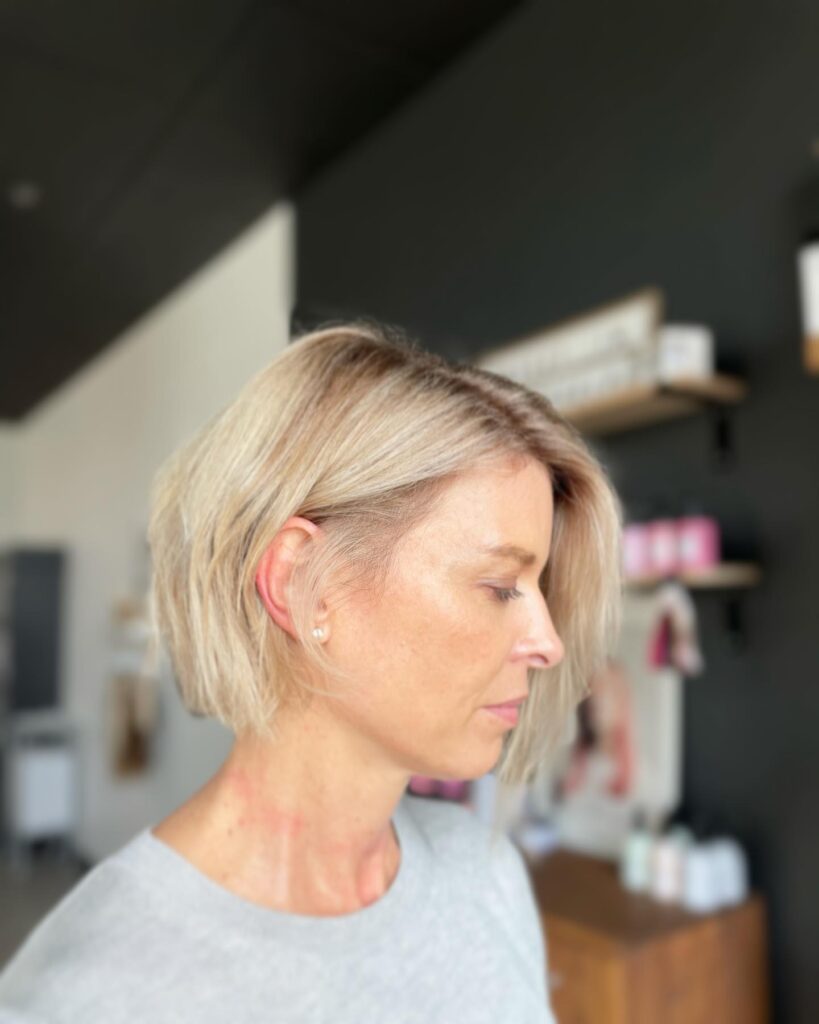 A woman looking down in side profile showcasing her straight, chin length vanilla blonde bob with choppy ends and one side tucked behind her ear.