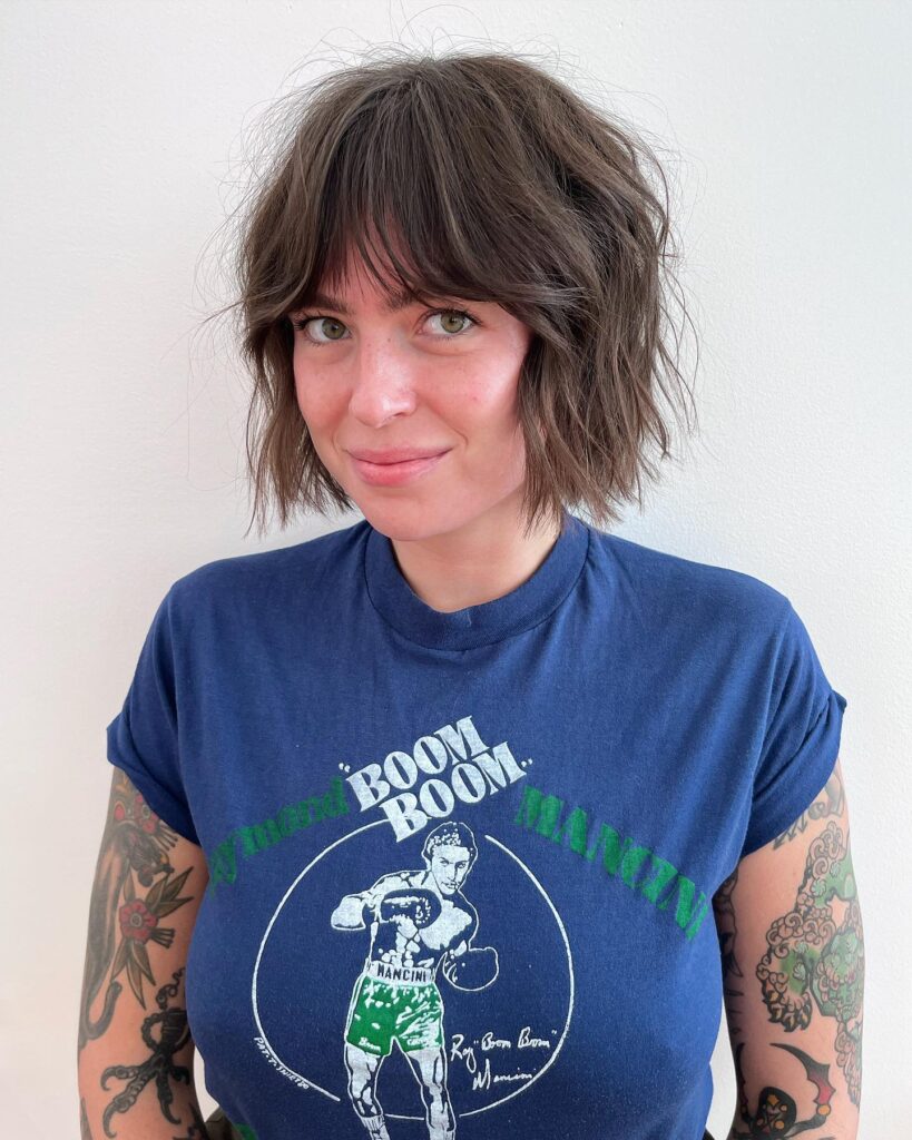 A smiling woman with a textured chin length brunette shag bob featuring messy layers and curtain bangs.