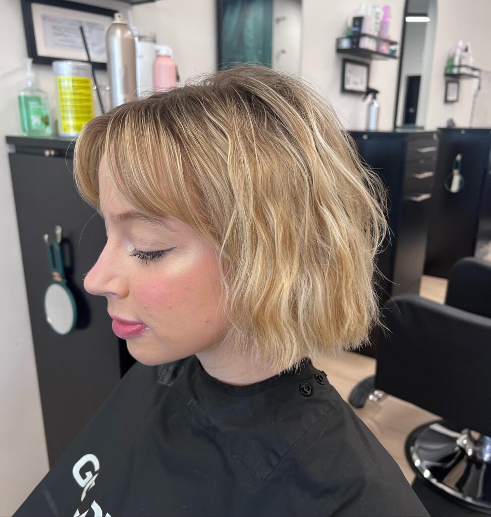 A woman showing the side profile of her beachy chin length golden blonde bob with textured layers and soft curtain bangs.
