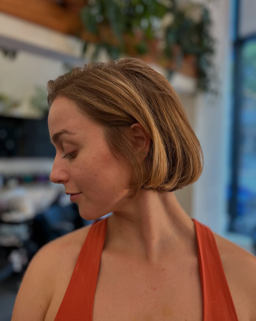 A woman looking down and showing the side profile of her smooth honey blonde chin length bob with one side tucked behind her ear.