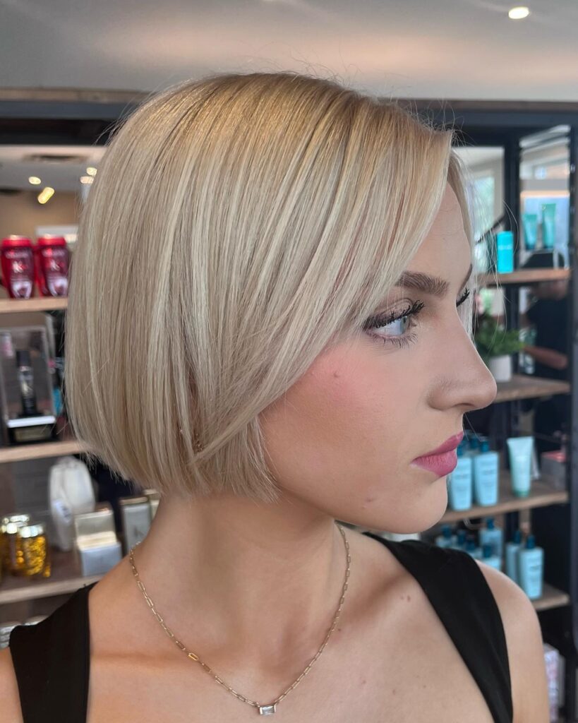 A woman looking to the side showcasing a smooth, straight chin length creamy blonde angled bob with subtle face framing layers.