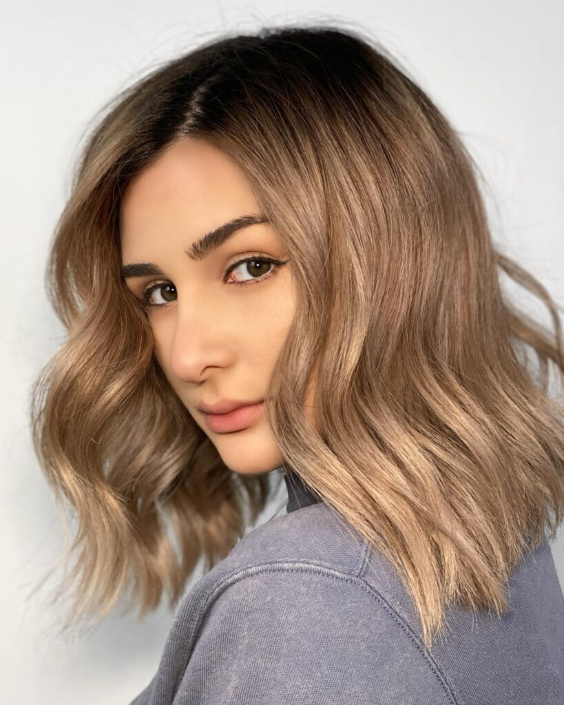 Wavy shoulder length long bob with soft beige blonde tones and natural texture.