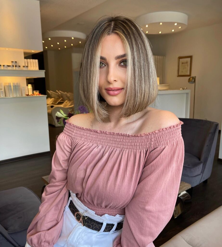 Sleek straight long bob with a blunt cut and soft blonde highlights parted in the center.