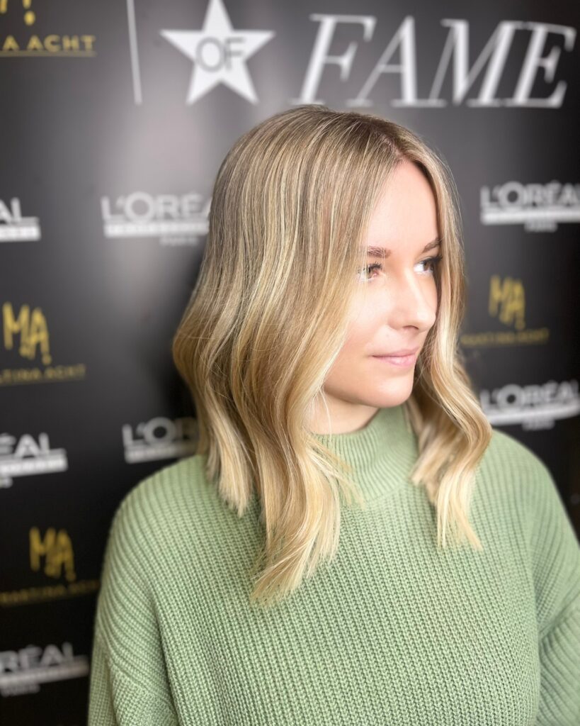 Shoulder length long bob with soft waves and warm blonde tones.