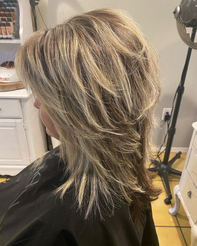 A woman with a heavily layered, voluminous choppy blonde shaggy bob hairstyle with long side-swept bangs.