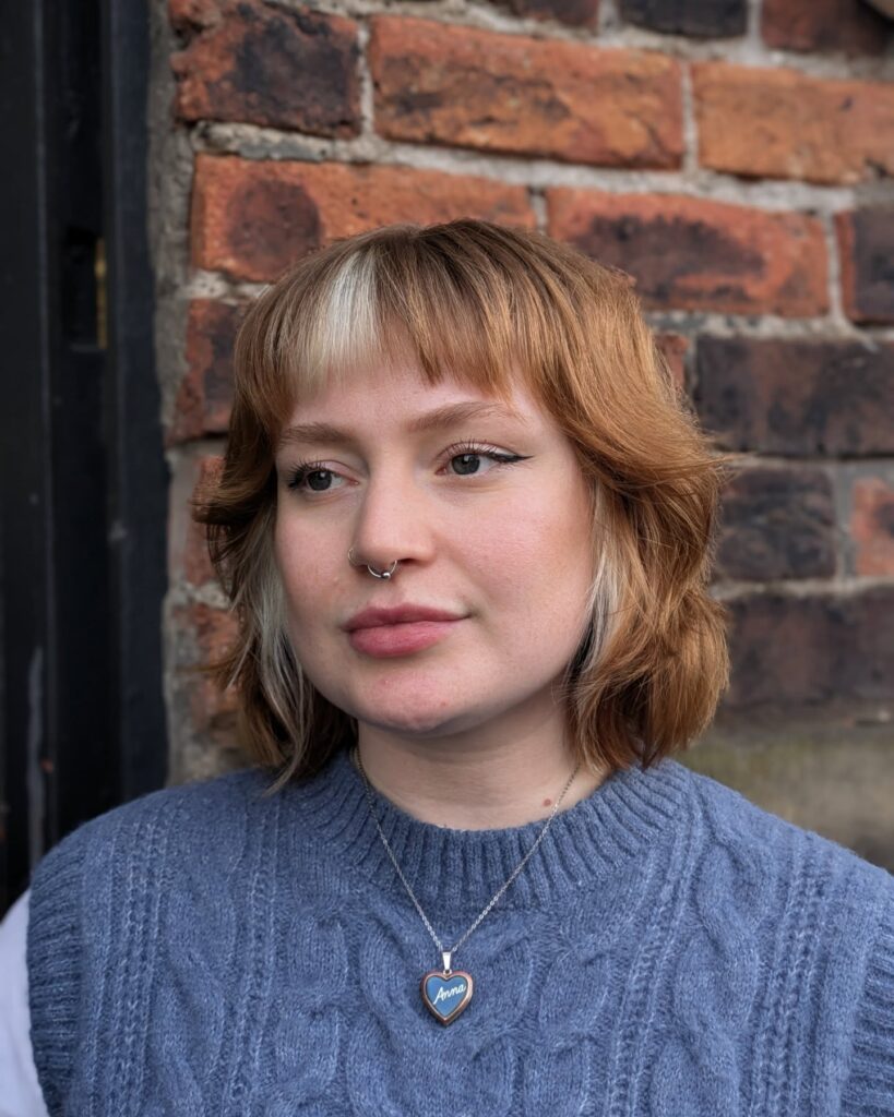 A woman with a copper-colored choppy bob featuring prominent platinum blonde highlights in her side-swept bangs and side layers.