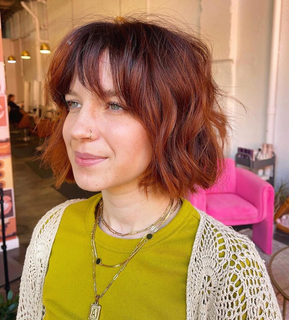 A woman looking forward showcasing a neck-length, texturized blonde lob haircut with sun-kissed highlights and relaxed side-swept bangs.