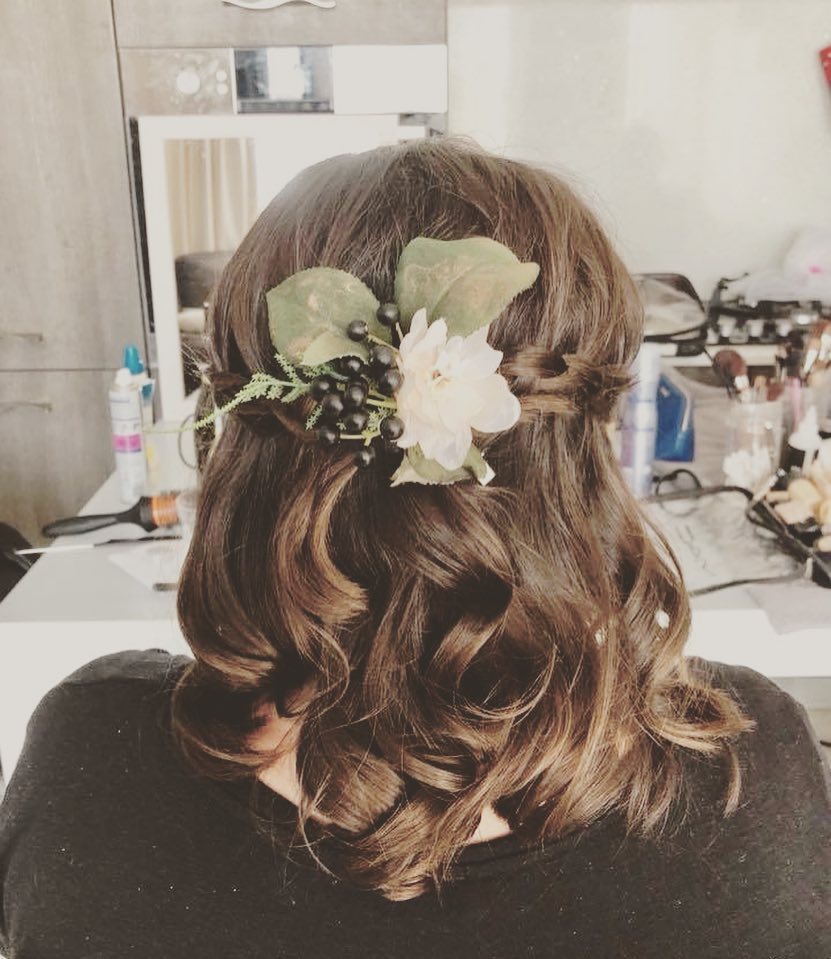 A back view of a brunette with a curly bob styled in a half-updo with a white flower and blackberry hair accessory.