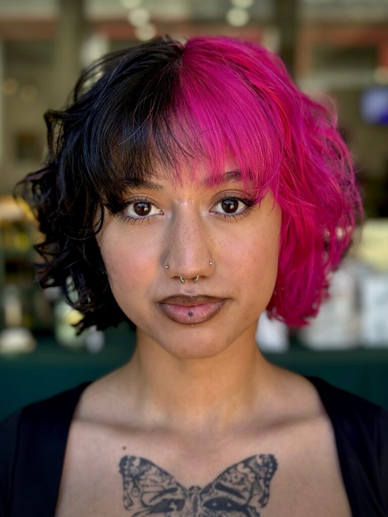 A woman with a split-dyed curly French bob in black and hot pink with matching bangs.