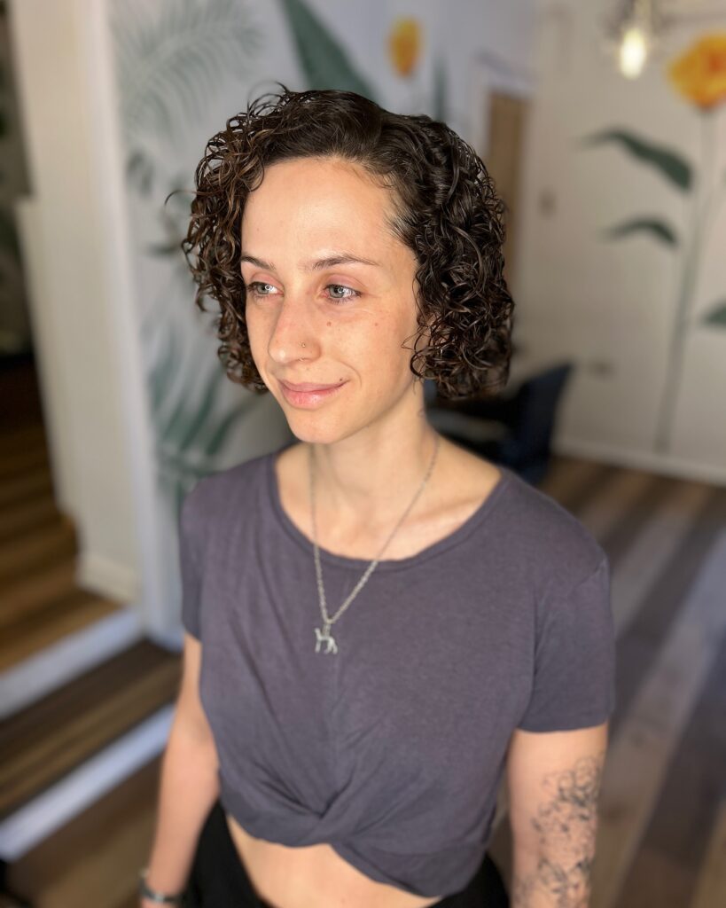 A woman with a dark walnut brown curly French bob featuring tight, defined ringlets and no bangs.