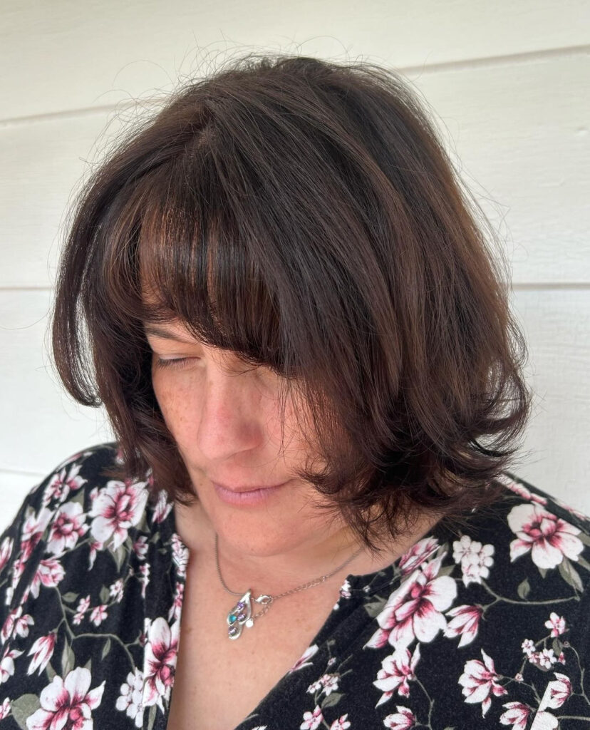 A woman with a collarbone-length espresso brown bob featuring flipped-out layers and a soft wispy fringe.