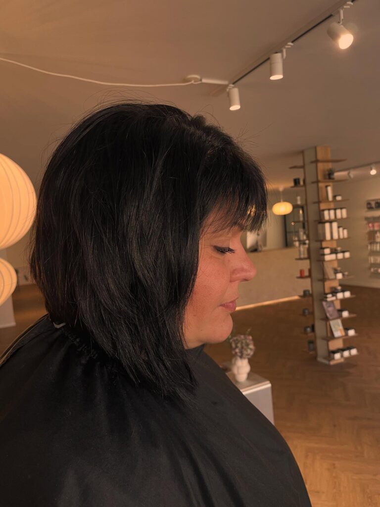 A woman with an angled midnight black layered bob featuring wispy bangs and tapered front sections.