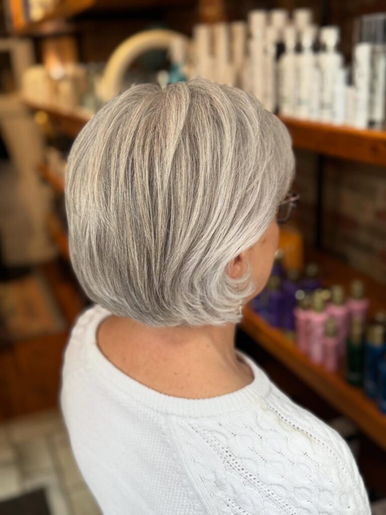 A woman from the back showing a neck-length feathered gray bob with voluminous layers and a rounded shape.