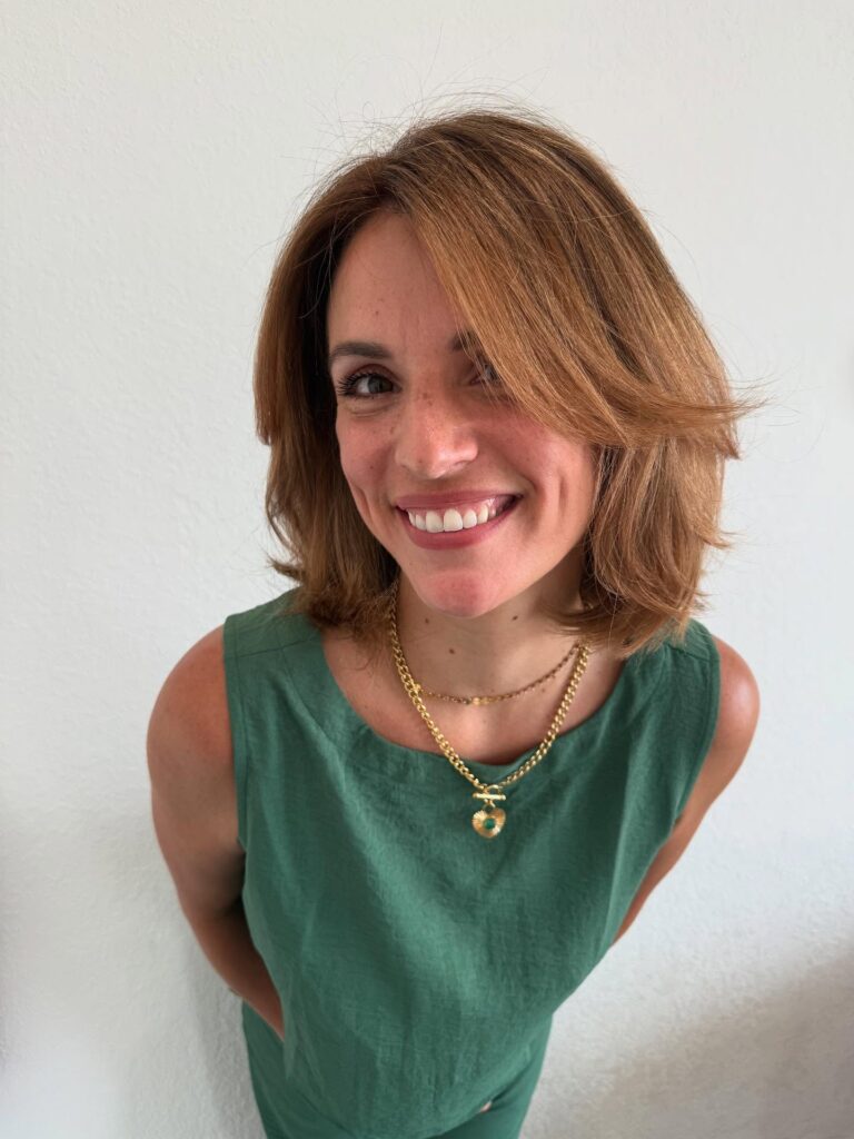 A smiling woman with a shoulder-length auburn bob featuring voluminous top layers and a side-swept fringe.