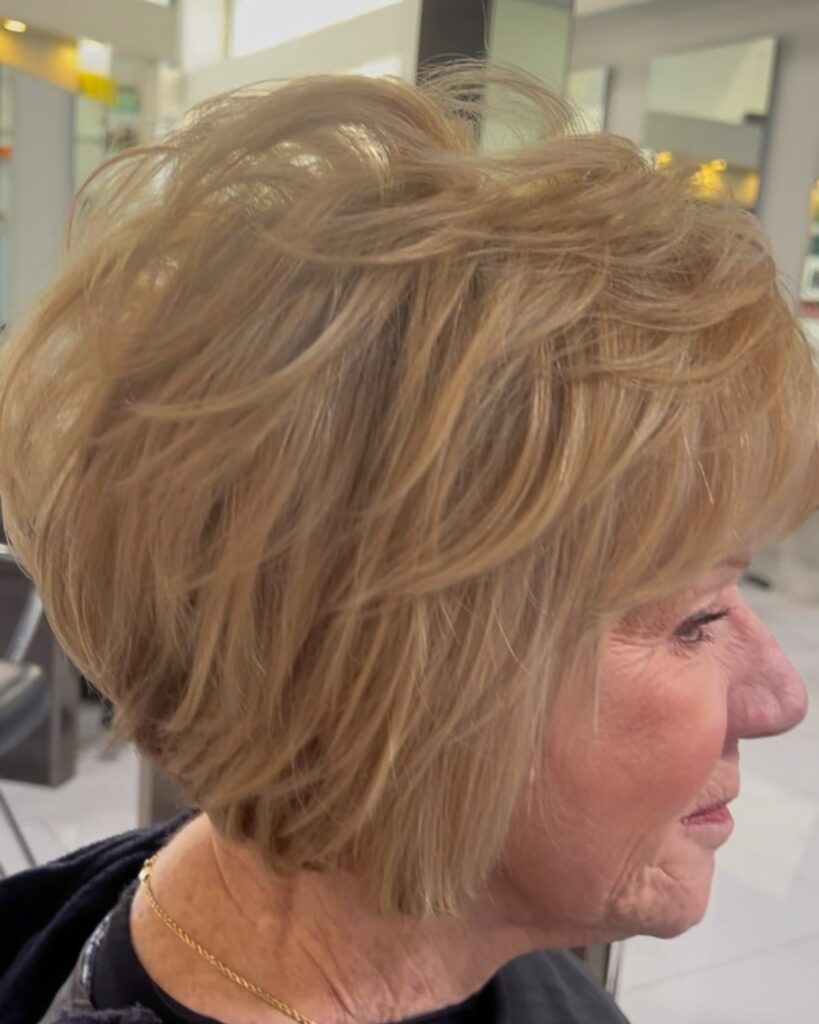 A woman in profile with a chin-length golden blonde bob featuring voluminous textured layers throughout the crown and back.
