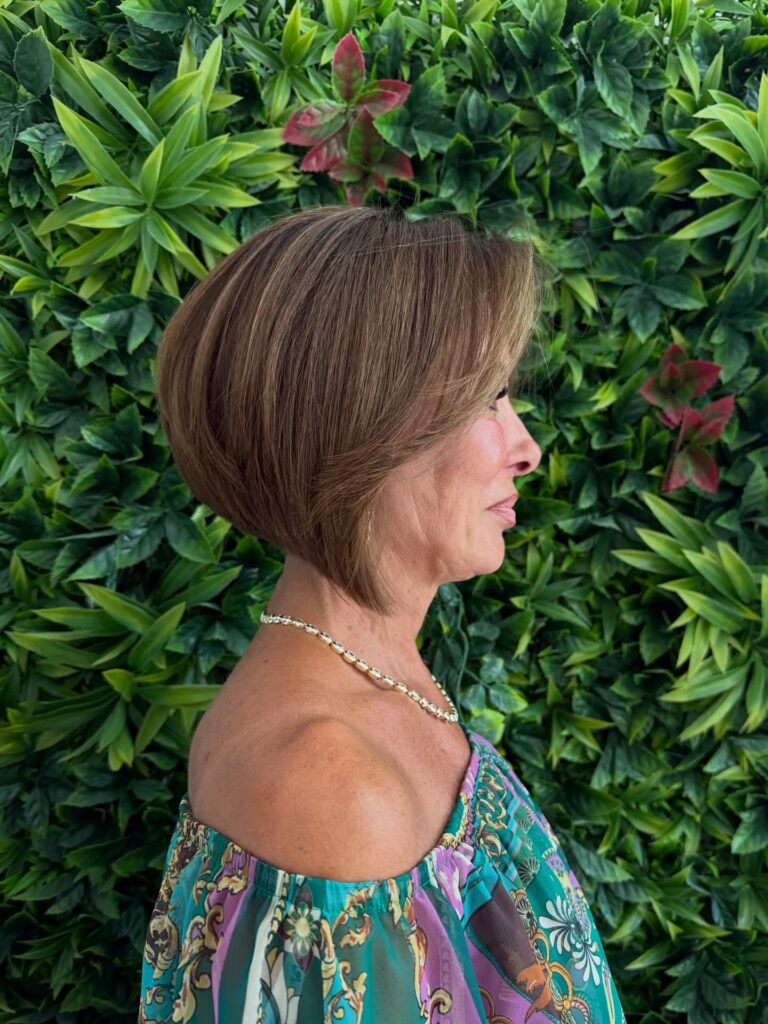 A woman in profile wearing a caramel brown stacked layered bob with a voluminous, rounded back and a sharp, angled front.