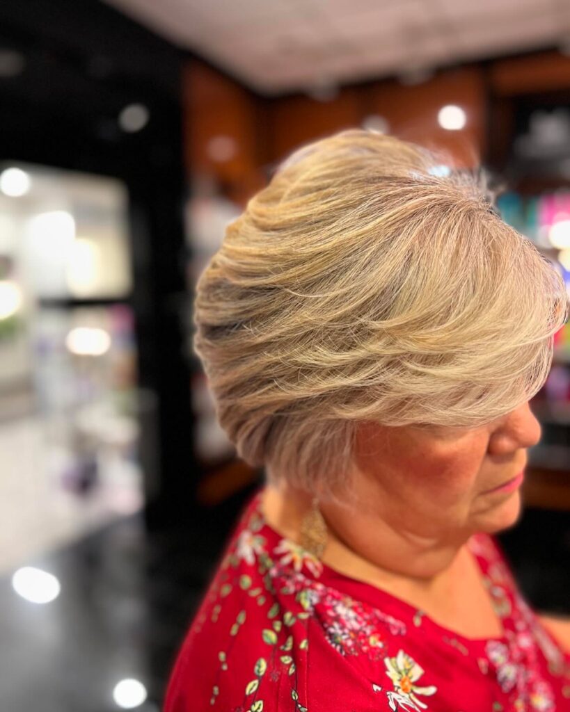 A woman showing a side profile of an ear-length champagne blonde bob with voluminous feathered layers swept back away from the face.