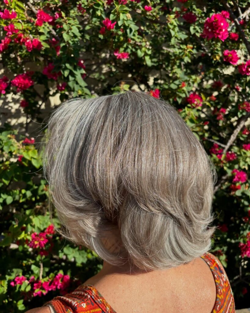 A woman from the back is showing a neck-length, silver, layered bob with ends flicked outward and soft, dimensional highlights.