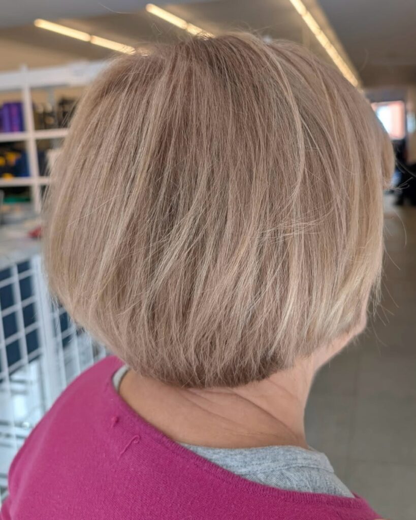 A woman with a chin-length champagne blonde mushroom bob featuring internal layers and a rounded silhouette.