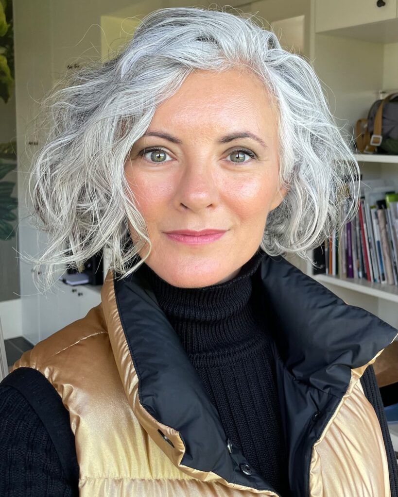 A woman with a chin-length voluminous silver layered bob featuring natural waves and a side part.