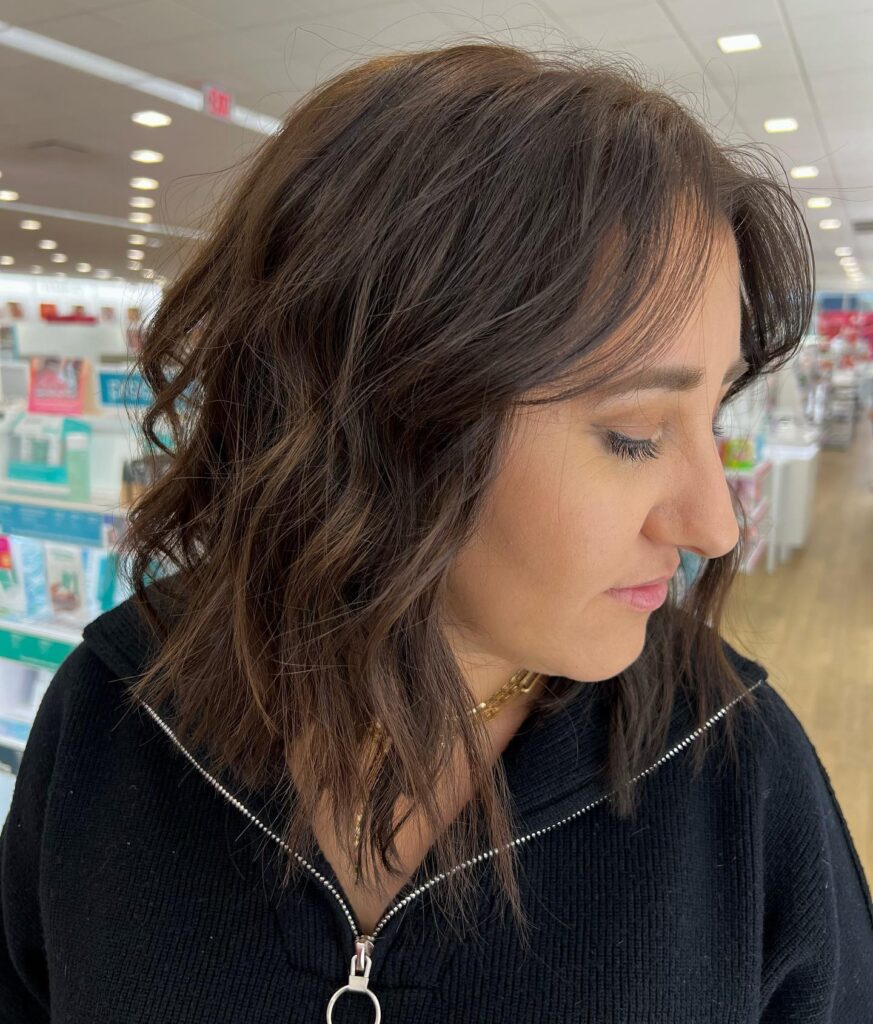 A woman with medium-length dark brown hair styled in messy waves with thin curtain bangs and an angled cut.
