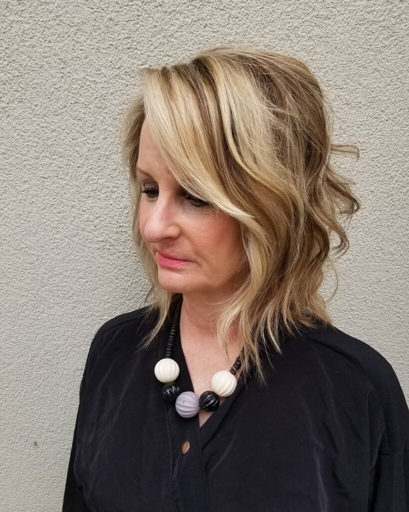 A woman with a shoulder-length angled bob in honey blonde featuring textured waves and a side-swept fringe.
