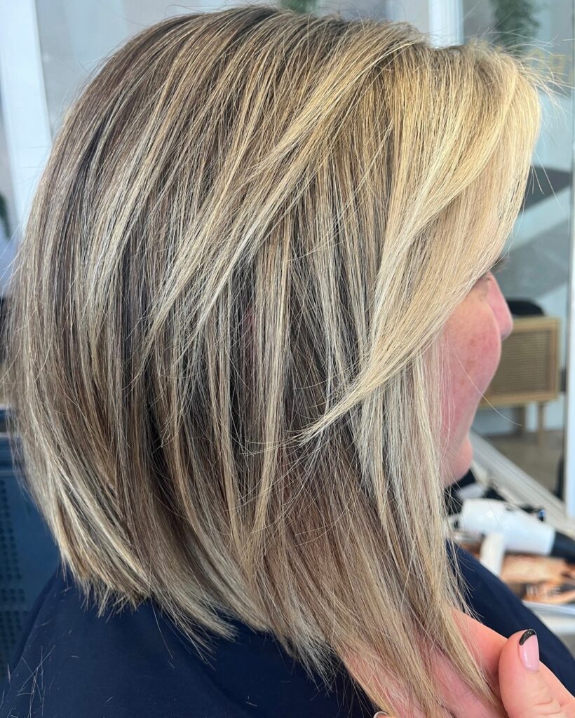A side profile of a textured, angled lob with heavy ash blonde highlights and feathered layers.