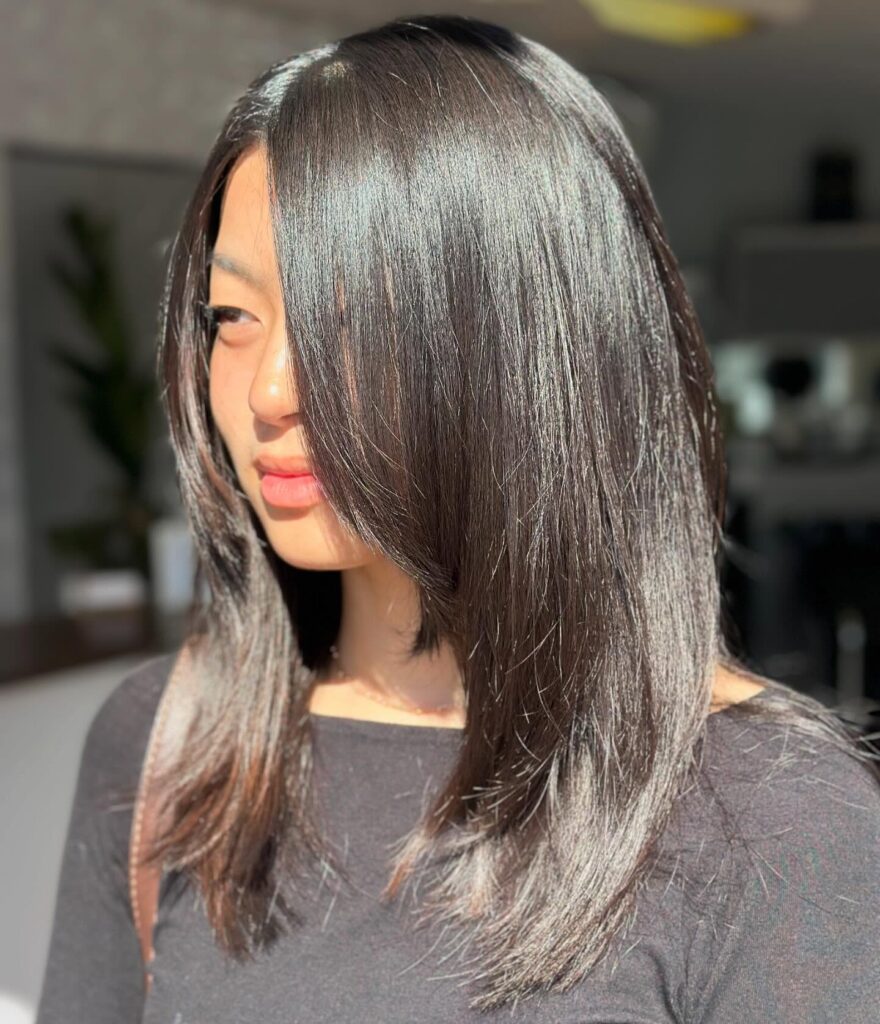 A woman with very shiny straight black hair styled in a long, angled bob with dramatic front layers.