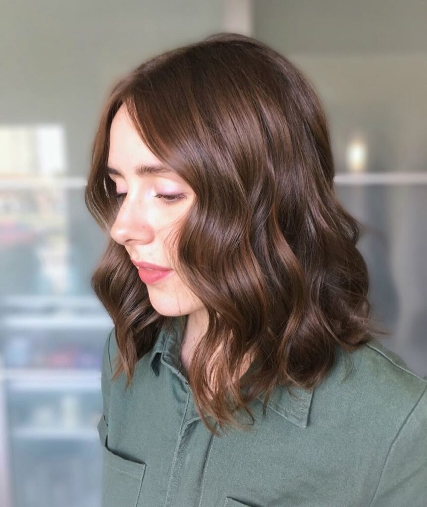 A woman with a middle-parted auburn angled long bob styled in soft glossy waves.