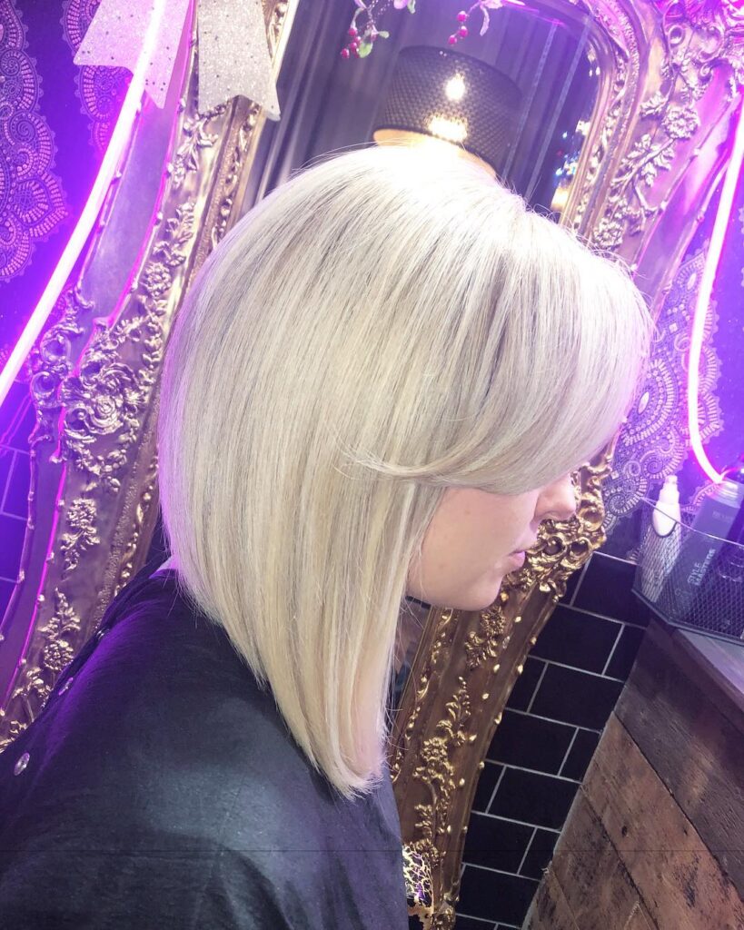 A side view of a woman with sleek, straight, icy blonde hair in a dramatic, angled long bob with side bangs.