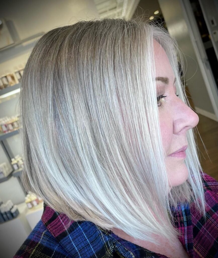 A side profile of a woman with a straight, icy silver, long bob featuring cool ash undertones.