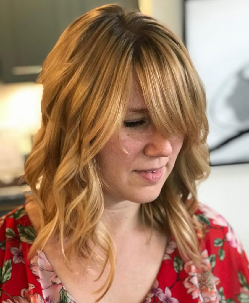 A woman with wavy strawberry blonde hair styled in an angled long bob with a long side-swept fringe.