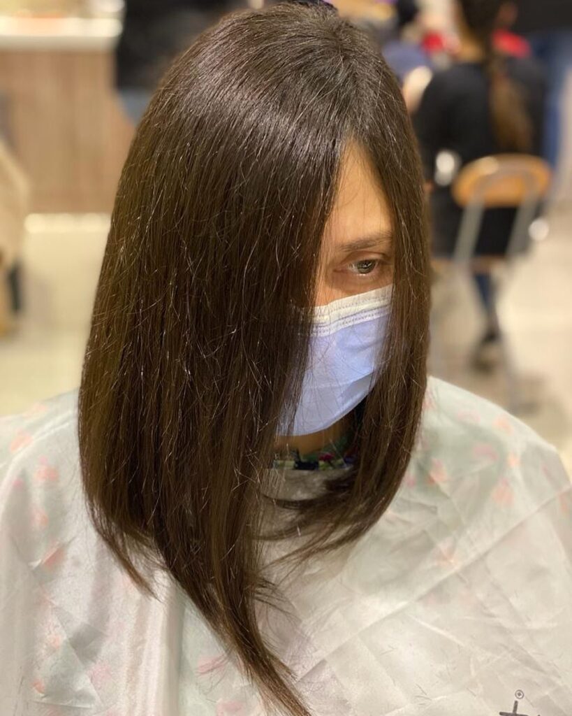 A woman with sleek, straight, dark brunette hair in a dramatic, angled long bob with long pointed front sections.