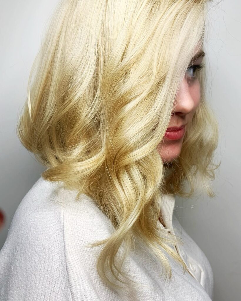 A woman with a side-parted bright blonde, long, angled bob styled in large, voluminous waves.