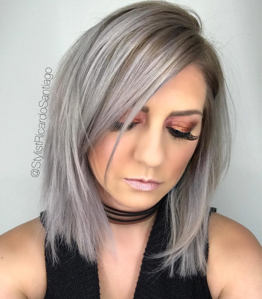 A woman with a side-parted, angled long bob featuring icy silver and lavender tones with a straight, piecey texture.