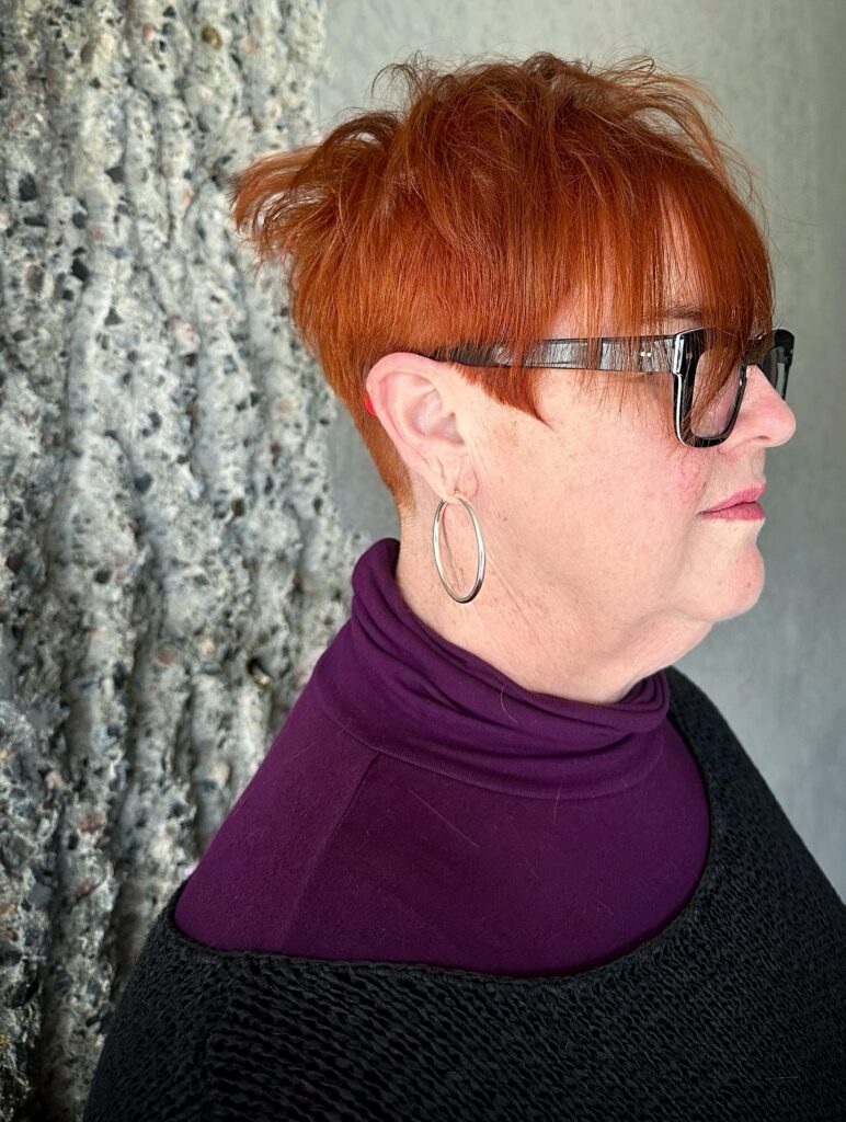 A woman wearing a vibrant copper red pixie cut with spiky layers on top and straight bangs.