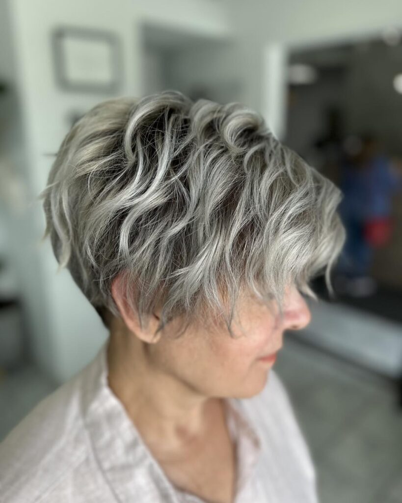A woman over 60 with a wavy salt-and-pepper pixie cut featuring long textured layers on top and a tapered back.